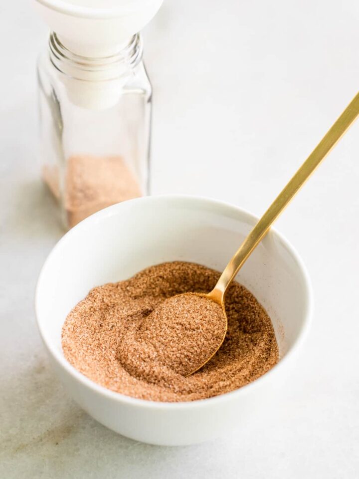 A bowl filled with cinnamon sugar with a spice jar on the side.