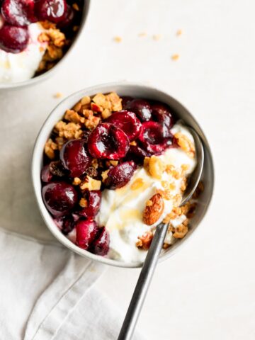 Bowl of yogurt topped with roasted cherries and granola.