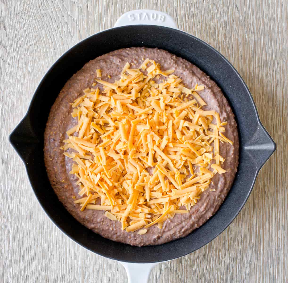 Unbaked black bean dip in skillet topped with cheddar cheese.