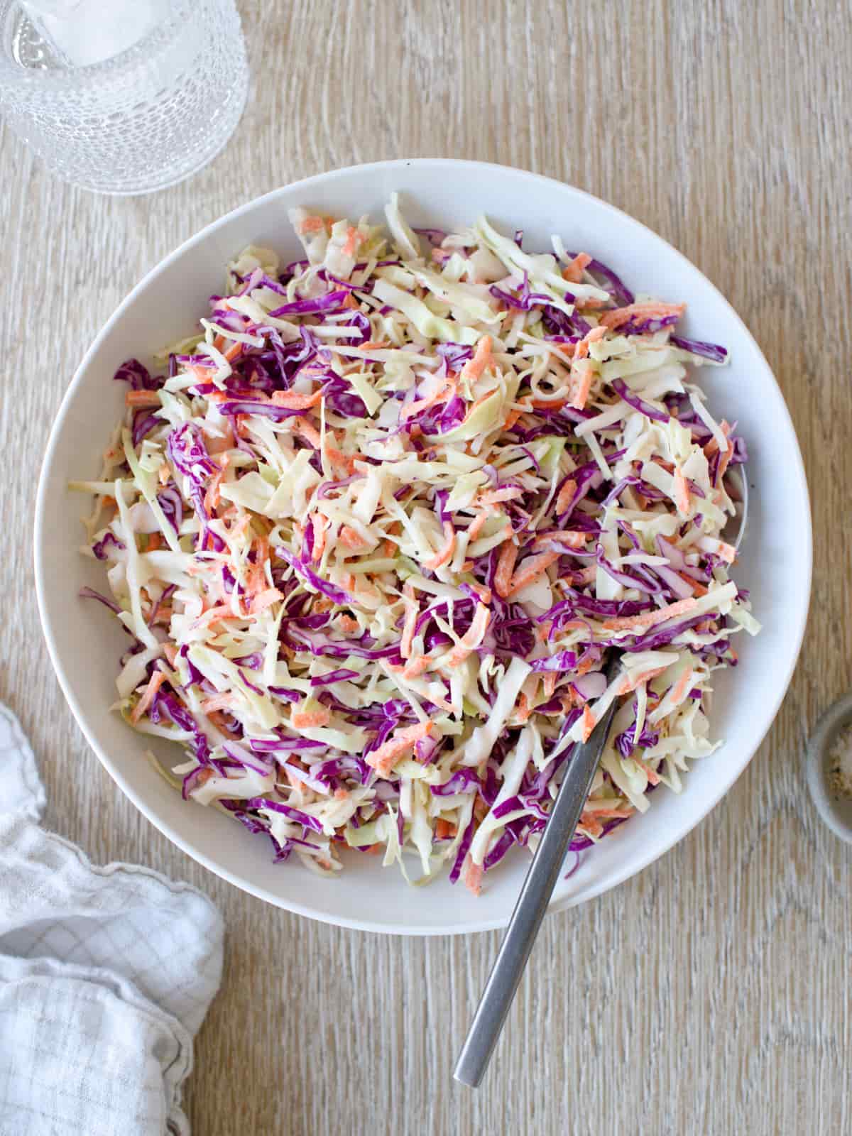 Bowl of coleslaw with glass of water and kitchen towel.