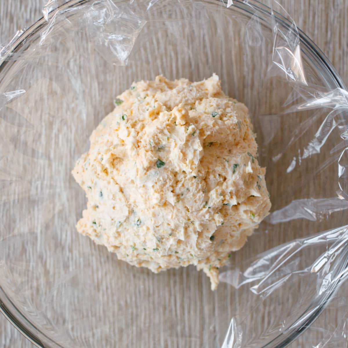 Cheese ball mixture in plastic wrap in bowl.