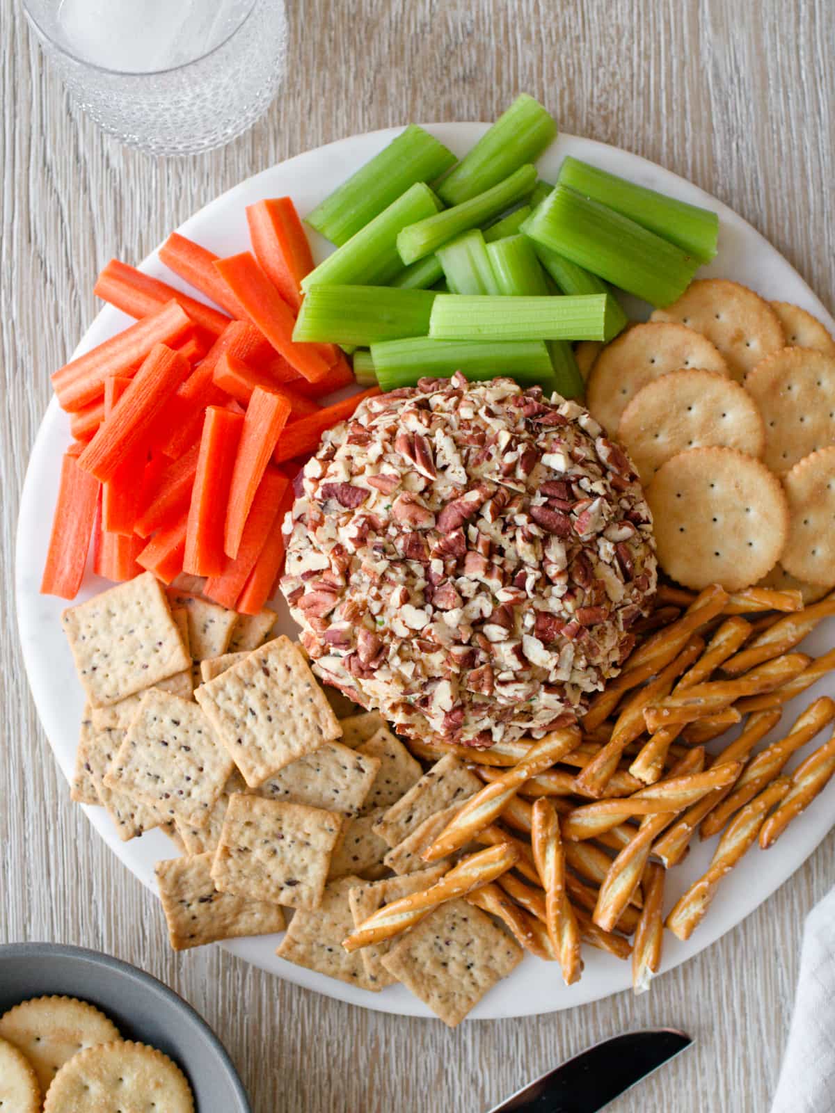 Cheese ball platter with vegetables, crackers, and a drink.