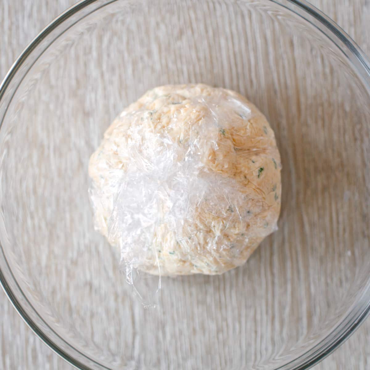 Cheese ball tightly wrapped in plastic wrap.
