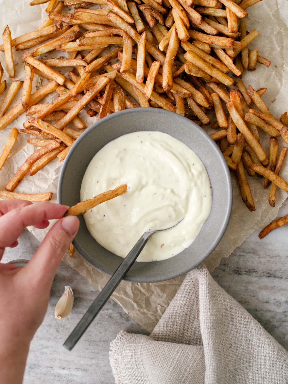 Hand dipping fries into bowl of garlic mayonnaise.