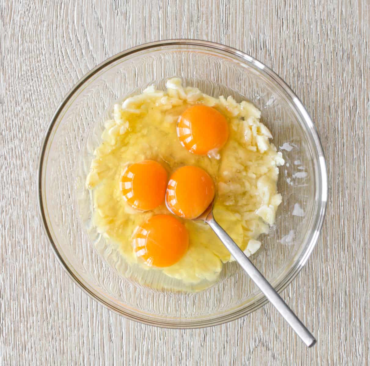 Mashed bananas with four eggs in medium bowl.