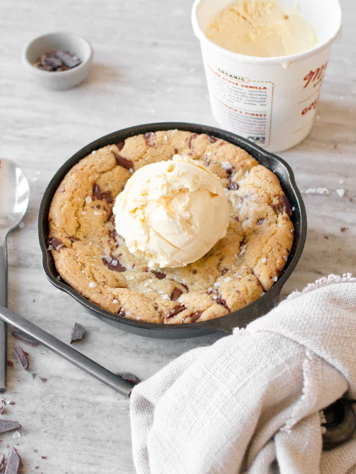 Mini skillet cookie with scoop of ice cream, ice cream pint, spoons, and towel.