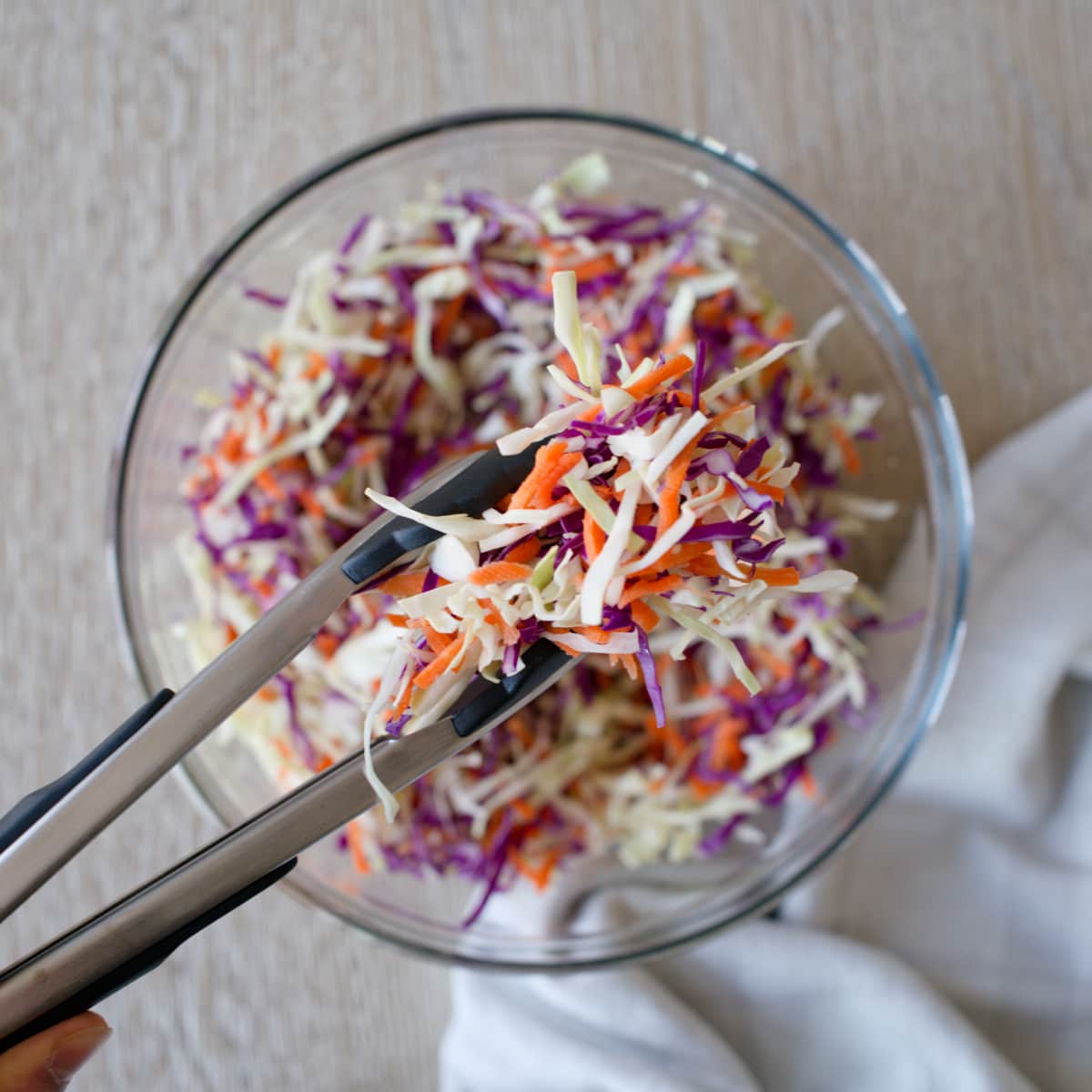 Mixing cabbages and carrots with a tong in a large bowl.
