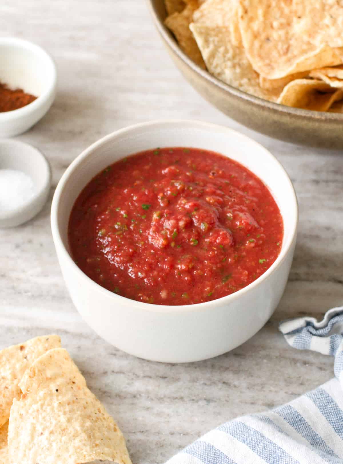 Bowl of homemade salsa with a bowl of ingredients and seasoning.