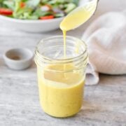 Spoon pouring honey mustard dressing in mason jar.
