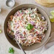 Bowl of taco slaw with stack of tortillas.