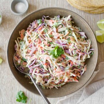 Bowl of taco slaw with stack of tortillas.