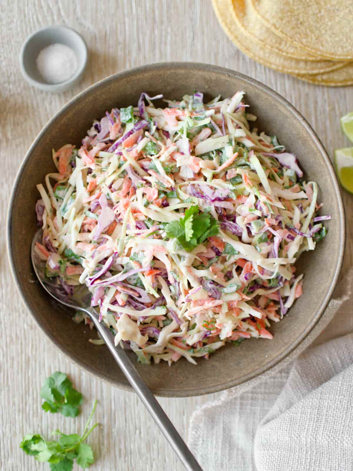 Bowl of taco slaw with stack of tortillas.