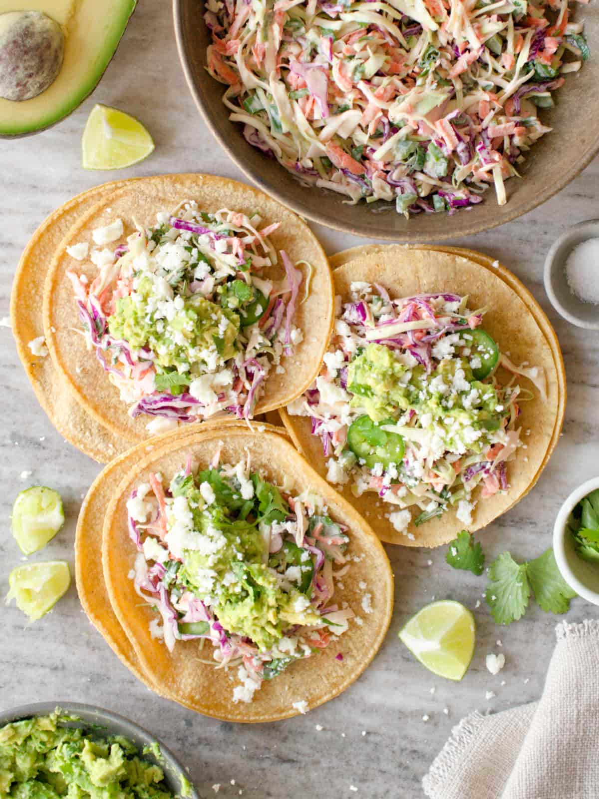 Three tacos with taco slaw and other toppings on them.