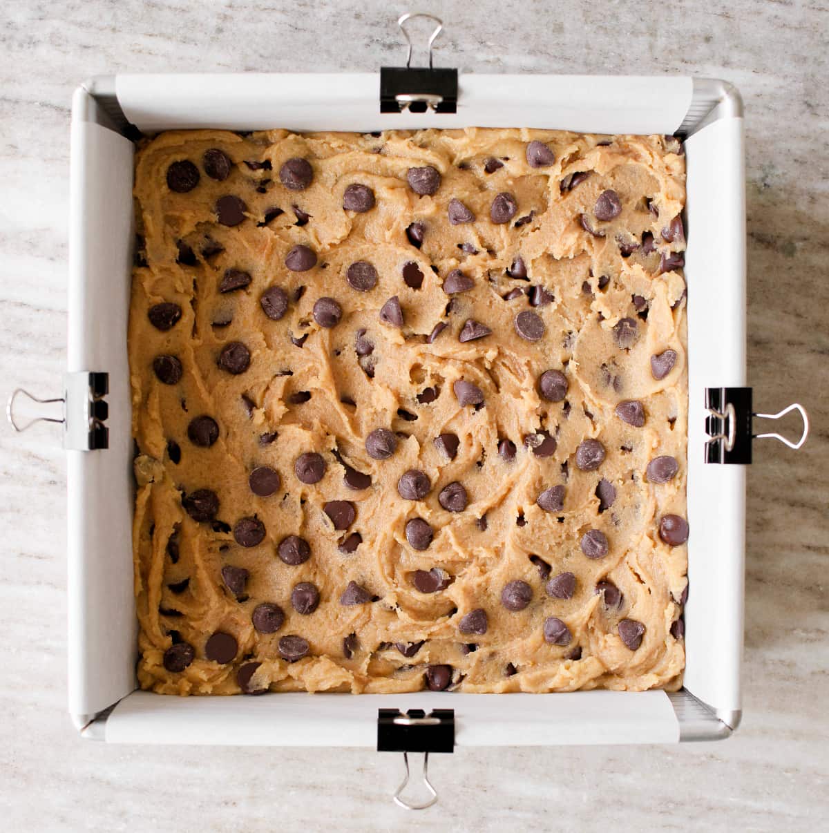 Cookie dough spread on square baking pan.
