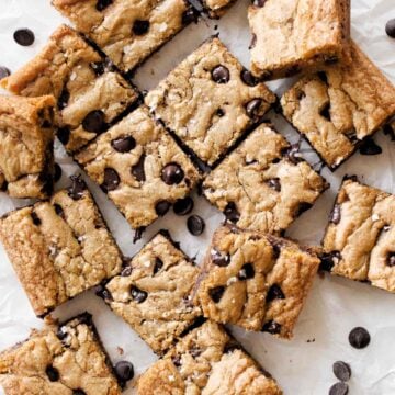 Chocolate chip cookie bars spread out on parchment paper.