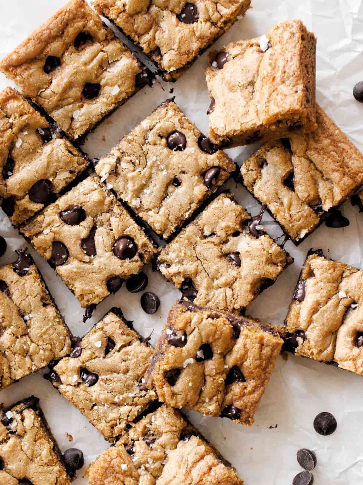 Chocolate chip cookie bars spread out on parchment paper.