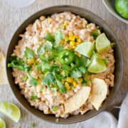Corn dip with garnishes and tortilla chips in bowl.