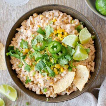 Corn dip with garnishes and tortilla chips in bowl.