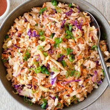Egg roll in a bowl with coleslaw mix and serving spoon.