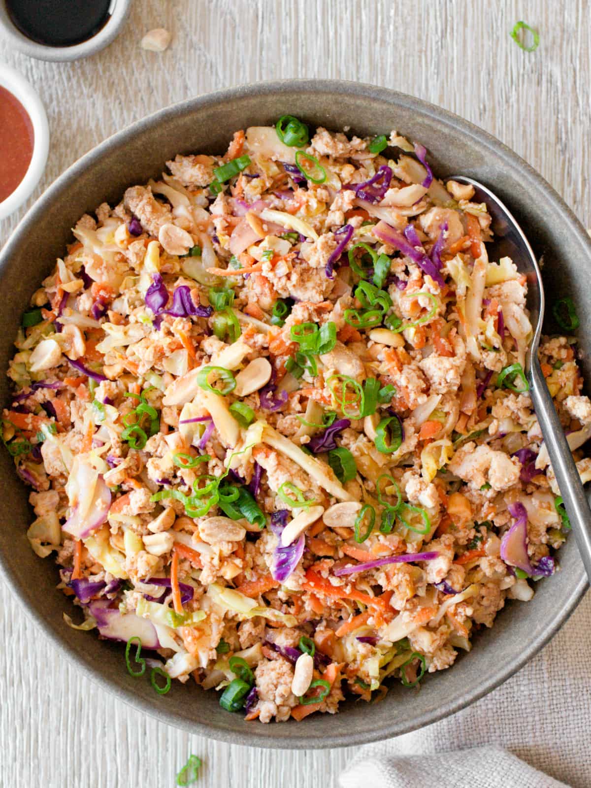 Egg roll in a bowl with coleslaw mix and serving spoon.