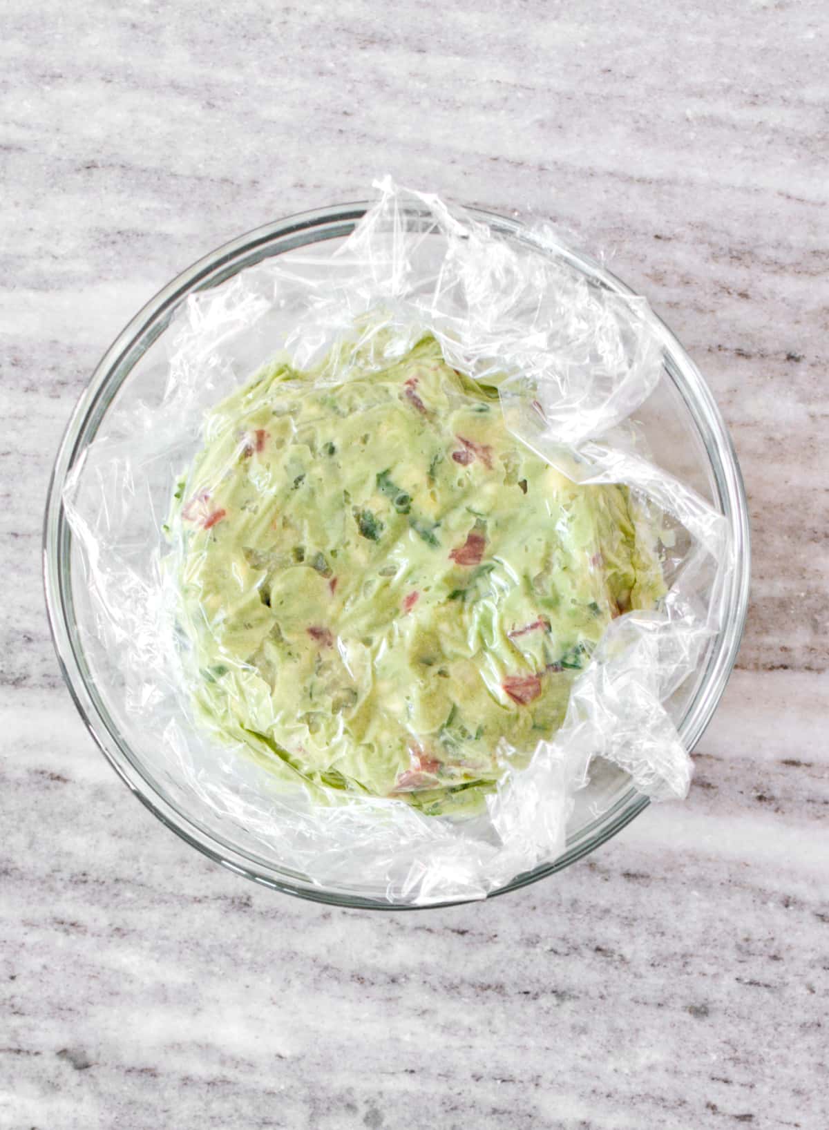 Fresh guacamole in bowl covered with plastic.