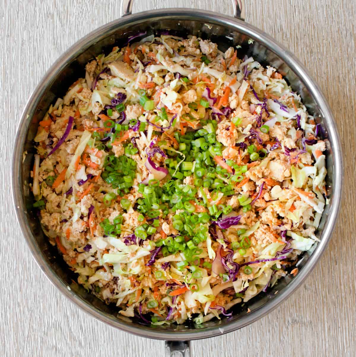 Coleslaw mix, green onions, and peanuts added to make egg roll in a bowl in the pan.