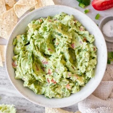Bowl of guacamole surrounded by tortilla chips and ingredients.