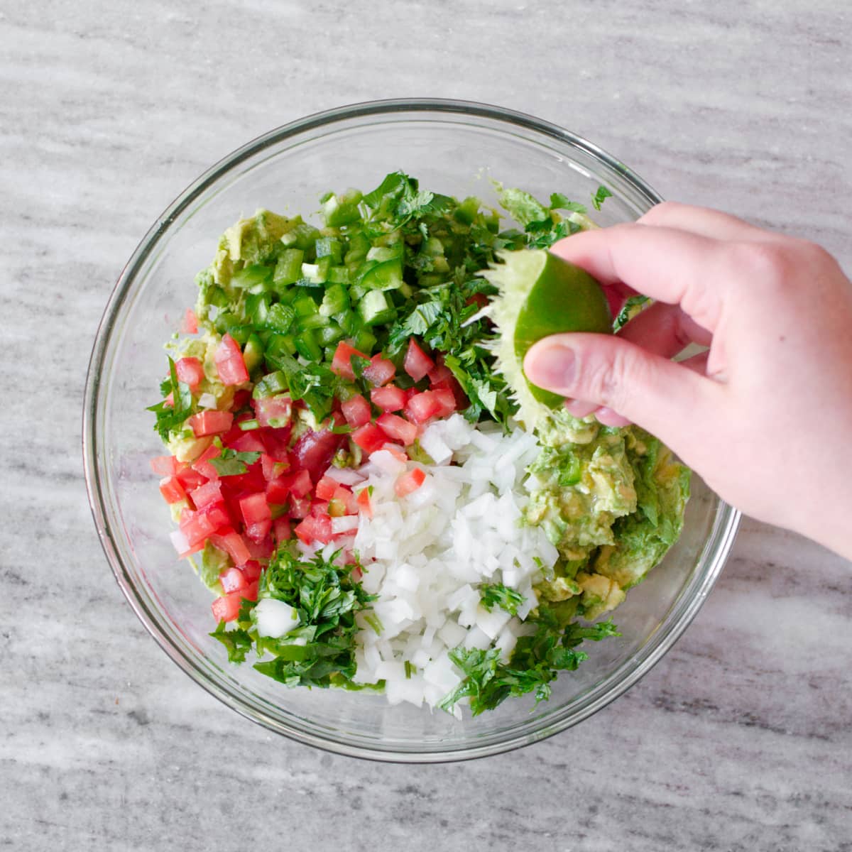 Squeezing lime into a bowl with smashed avocado and other ingredients.