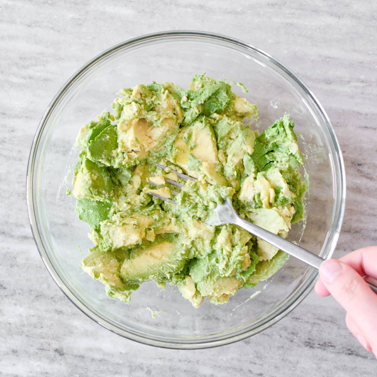 Smashing avocados in large glass bowl with fork.