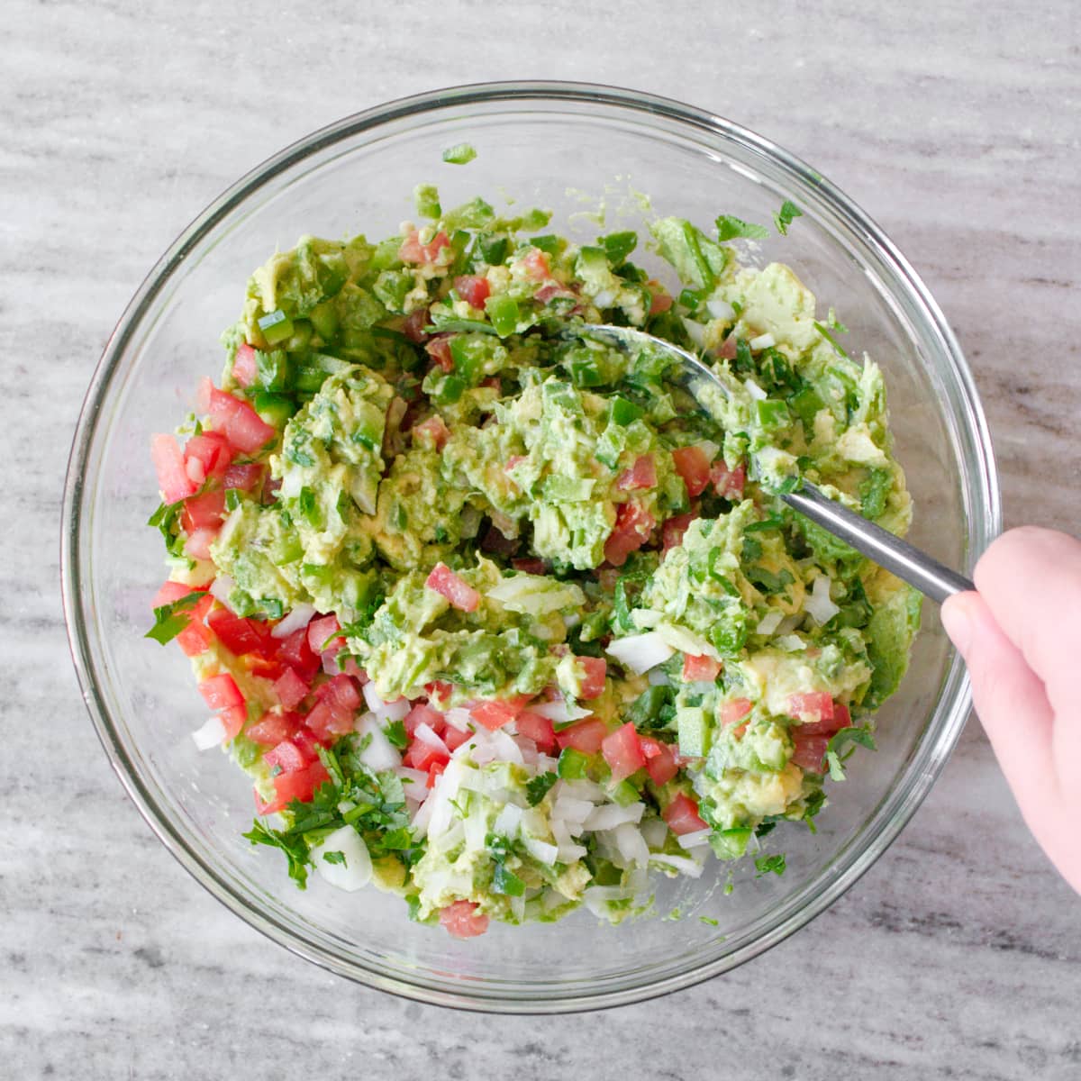 Mixing ingredients for guacamole in large glass bowl.