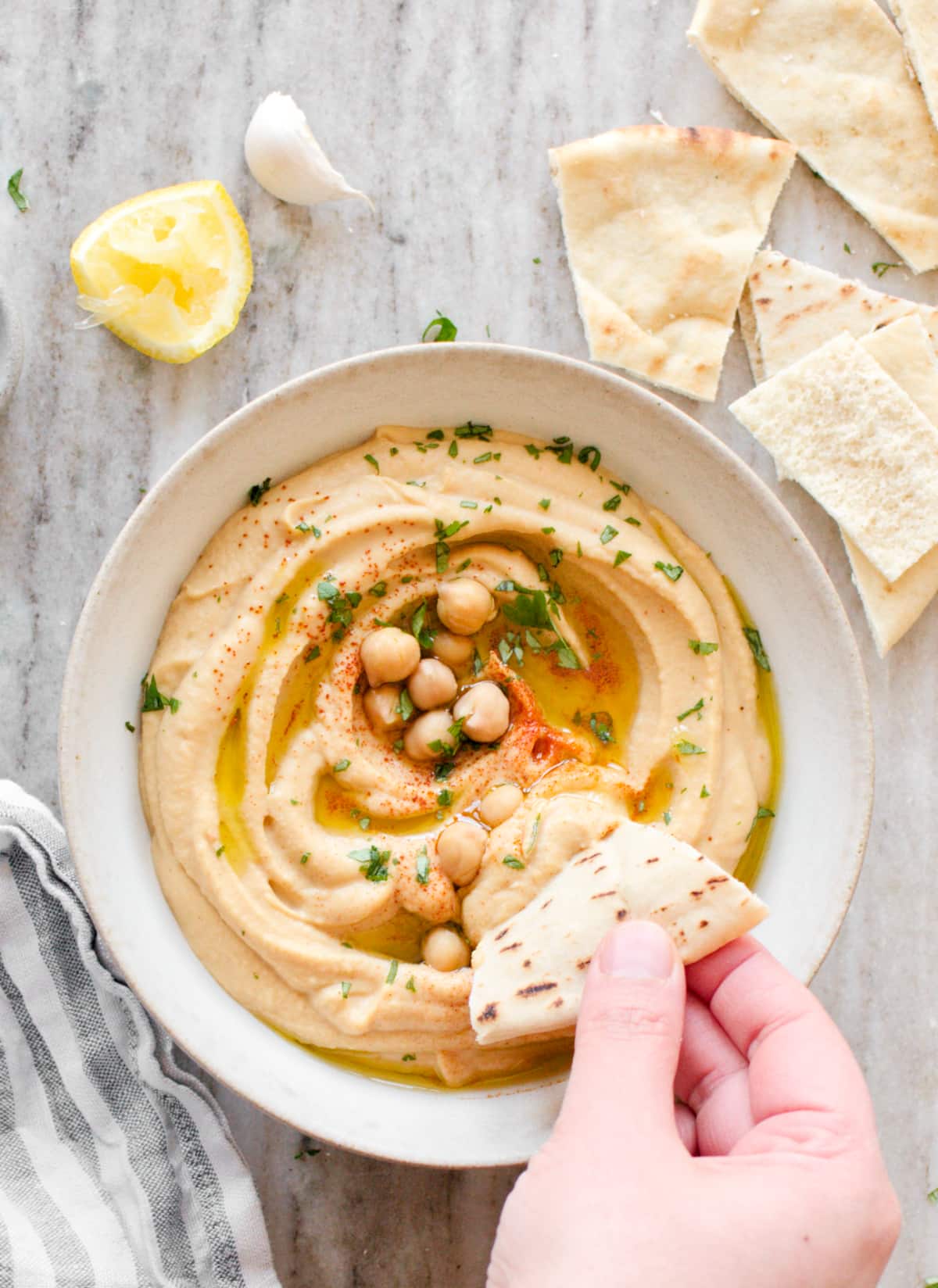Hand scooping hummus with pita bread.