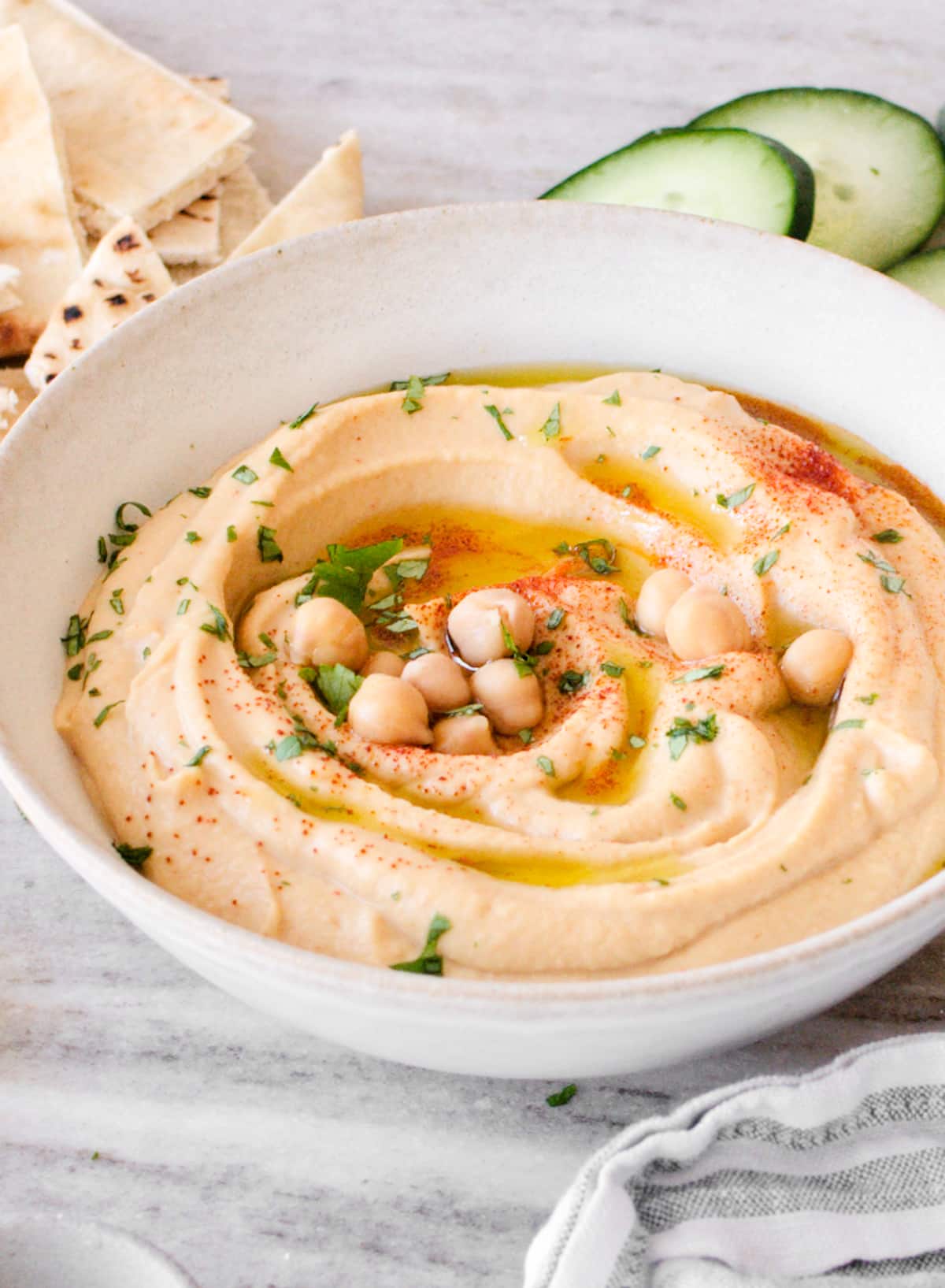 Bowl of hummus with pita bread, cucumber slices, and towel.