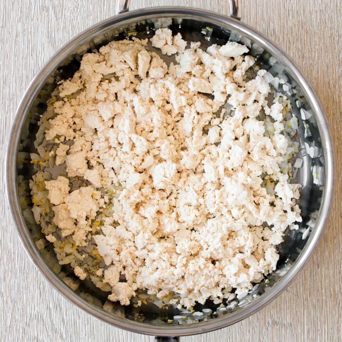 Tofu mixed with aromatics cooking in pan.