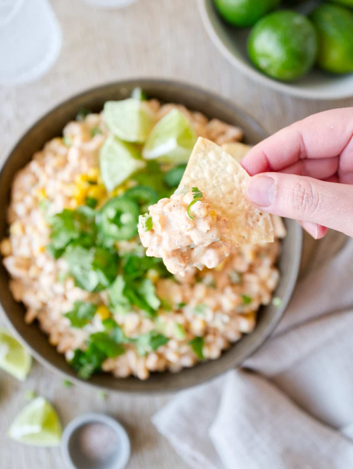 Hand scooping corn dip with a tortilla chip.