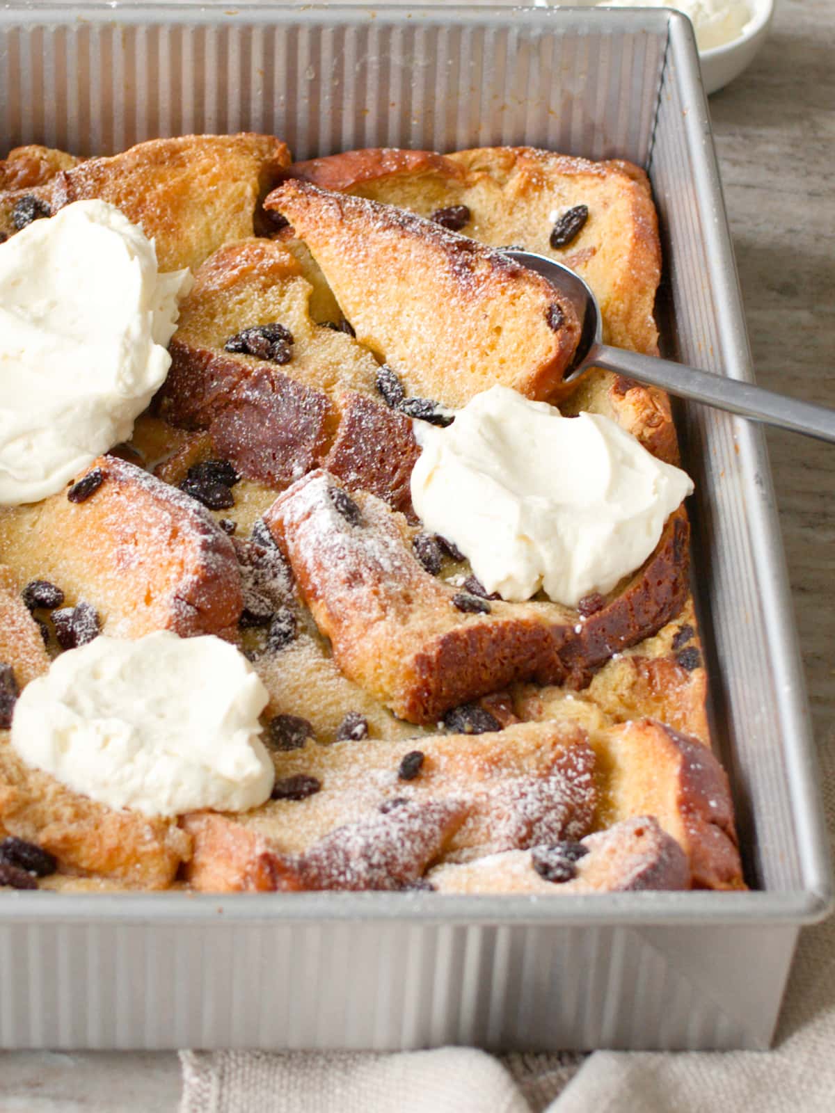 Spoon scooping out some bread and butter pudding from the baking dish.