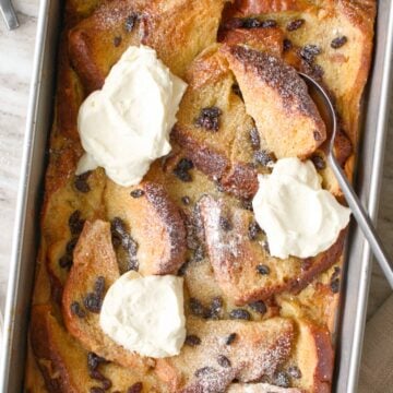 Bread and butter pudding with whipped cream in baking dish.
