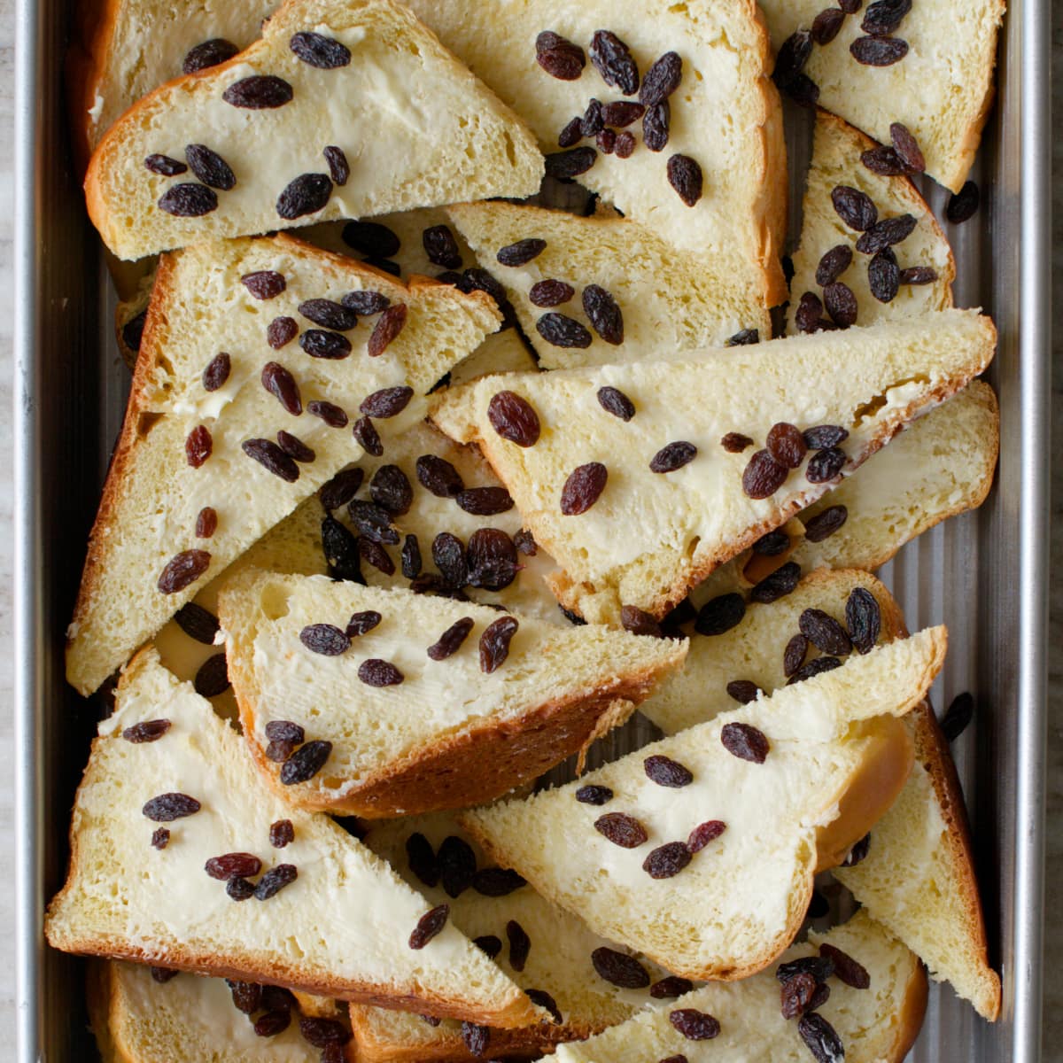 Slices of buttered bread and raisins in baking dish.