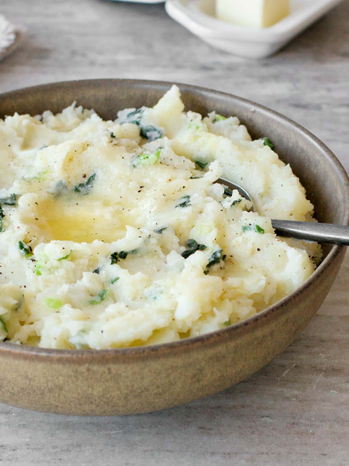 Side angle of colcannon in serving bowl with a butter dish.
